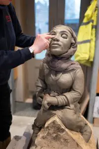A clay sculpture of Queen Æthelflæd, a stone mason works on the details around the eyes. 